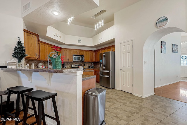 kitchen with arched walkways, a peninsula, visible vents, appliances with stainless steel finishes, and decorative backsplash