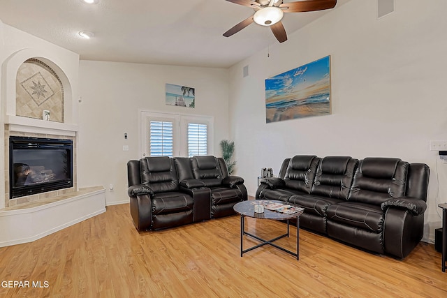 living area featuring a tiled fireplace, light wood-type flooring, a ceiling fan, and baseboards