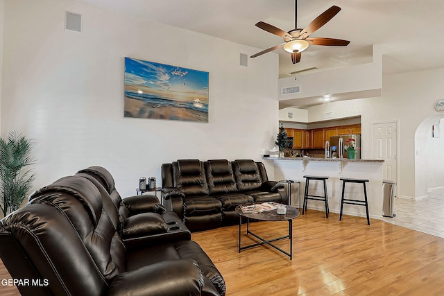 living area with light wood-type flooring, arched walkways, visible vents, and a ceiling fan