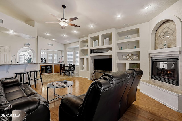 living room featuring built in features, lofted ceiling, a ceiling fan, light wood-type flooring, and a tile fireplace