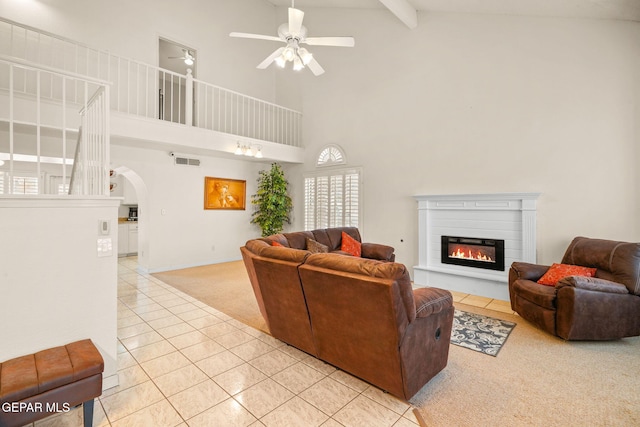 living area featuring light tile patterned floors, visible vents, arched walkways, a glass covered fireplace, and light colored carpet