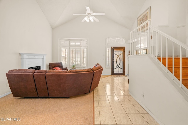 living area featuring a ceiling fan, high vaulted ceiling, light tile patterned flooring, a fireplace, and stairs