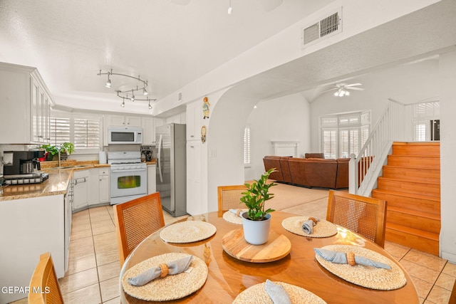 dining room featuring visible vents, a ceiling fan, arched walkways, light tile patterned flooring, and stairs