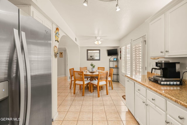 kitchen with arched walkways, stainless steel fridge, white cabinetry, and light tile patterned flooring