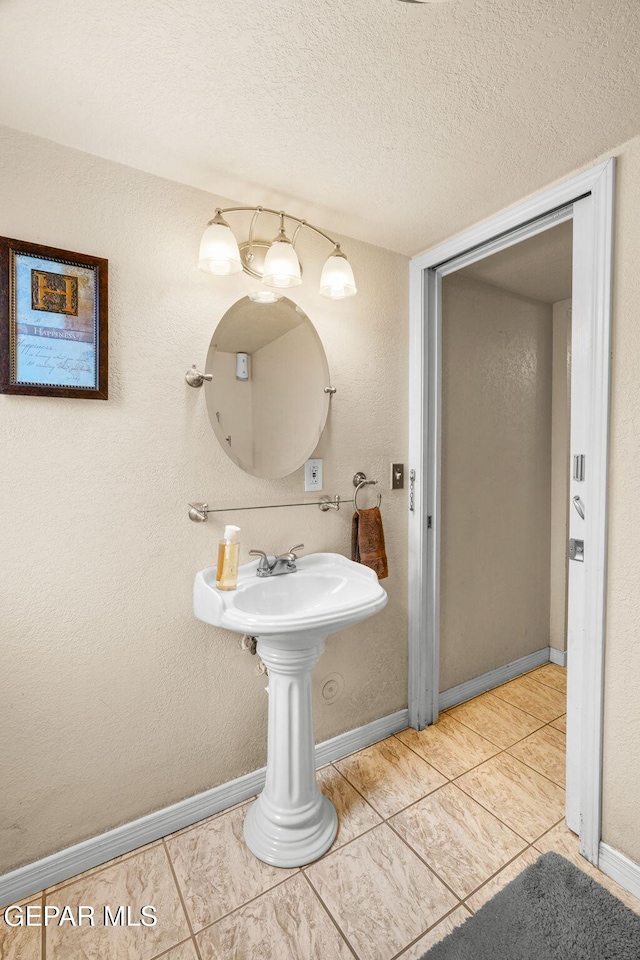 bathroom with tile patterned flooring, a textured ceiling, baseboards, and a textured wall