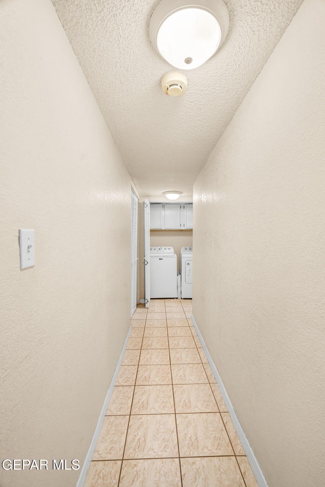 hallway with baseboards, washing machine and clothes dryer, light tile patterned flooring, a textured ceiling, and a textured wall