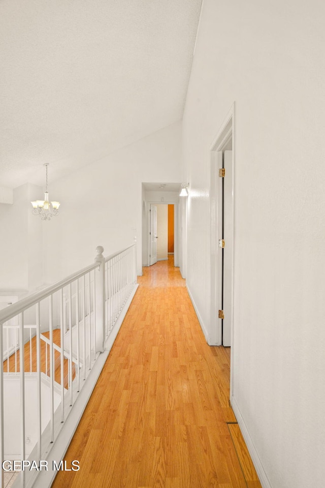 hall with baseboards, lofted ceiling, light wood-style floors, and an inviting chandelier