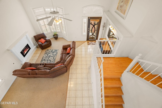 interior space with baseboards, a warm lit fireplace, ceiling fan, and tile patterned flooring