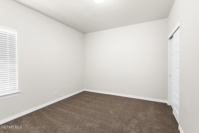 empty room featuring baseboards and dark colored carpet