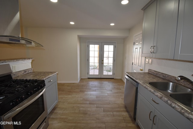 kitchen with wall chimney exhaust hood, appliances with stainless steel finishes, light wood-style floors, a sink, and recessed lighting