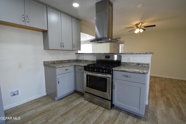 kitchen with stainless steel range with gas cooktop, gray cabinets, island range hood, light wood-type flooring, and a peninsula