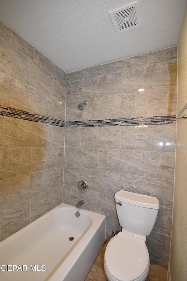 bathroom with toilet, a textured ceiling, tub / shower combination, and visible vents