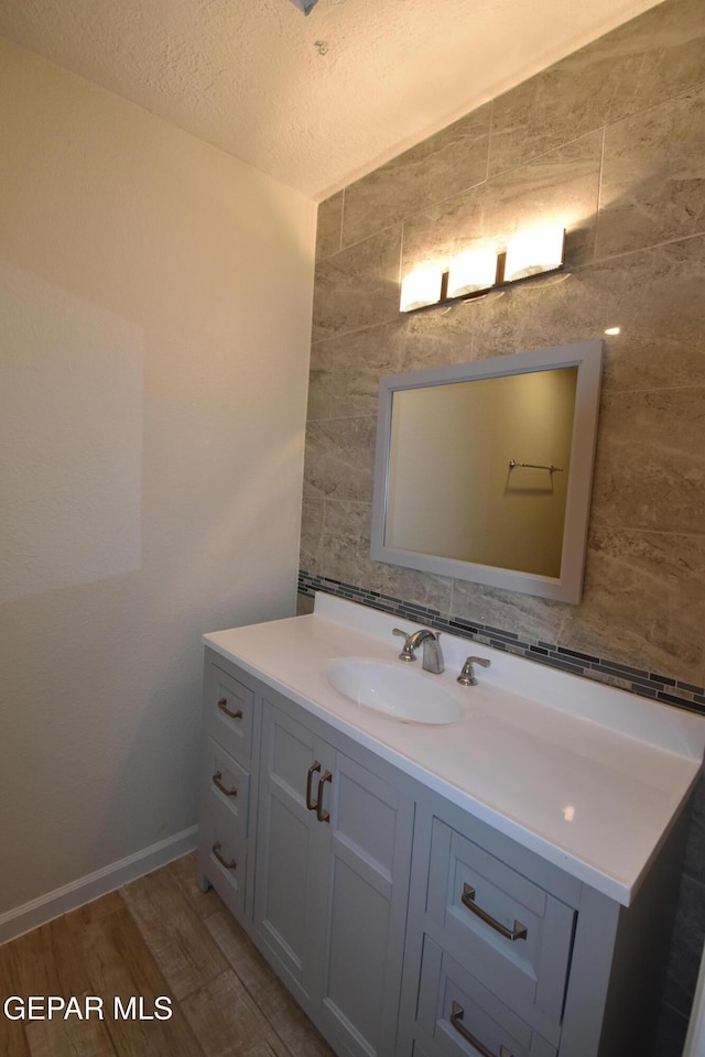 bathroom with a textured ceiling, wood finished floors, vanity, baseboards, and backsplash