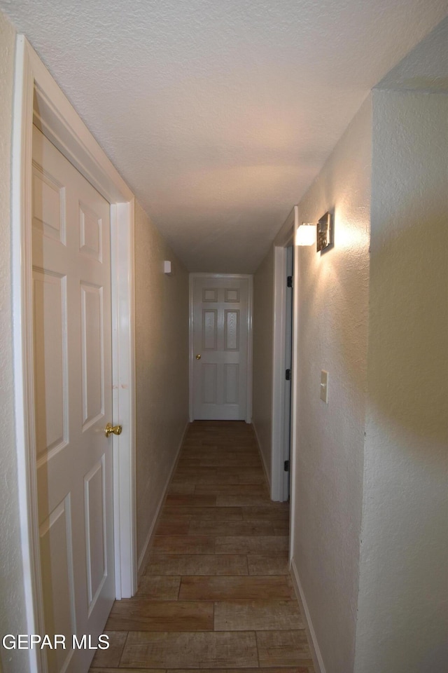 corridor featuring a textured wall, baseboards, and wood finished floors