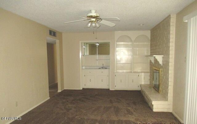 unfurnished living room with a fireplace, visible vents, dark colored carpet, and a textured ceiling