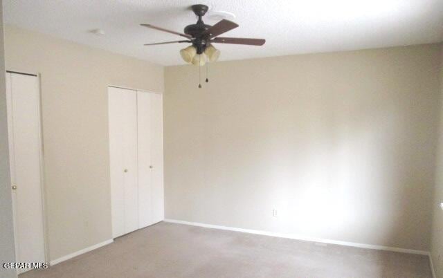 unfurnished bedroom featuring a ceiling fan, carpet, baseboards, and two closets