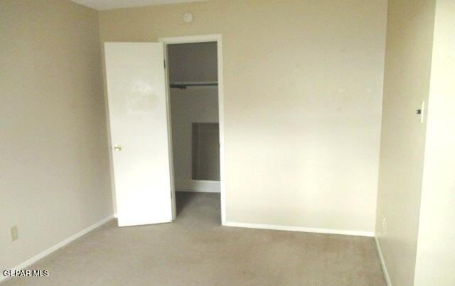 unfurnished bedroom featuring a closet, carpet flooring, a walk in closet, and baseboards