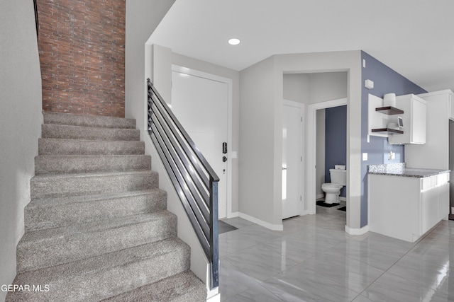 stairway with brick wall, marble finish floor, and baseboards