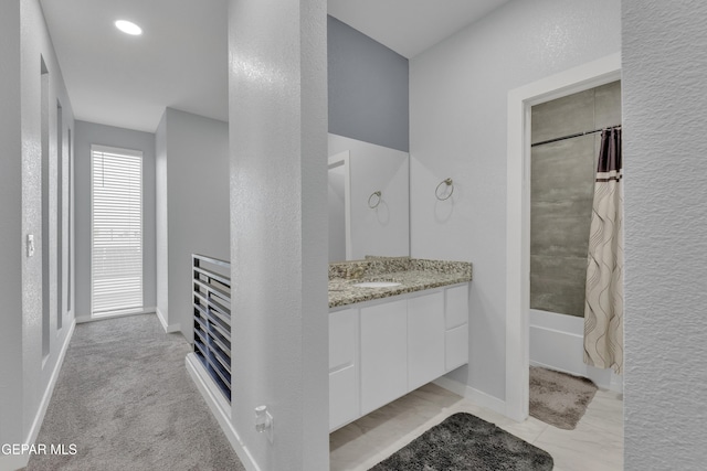 bathroom with shower / bathtub combination with curtain, a textured wall, vanity, and baseboards