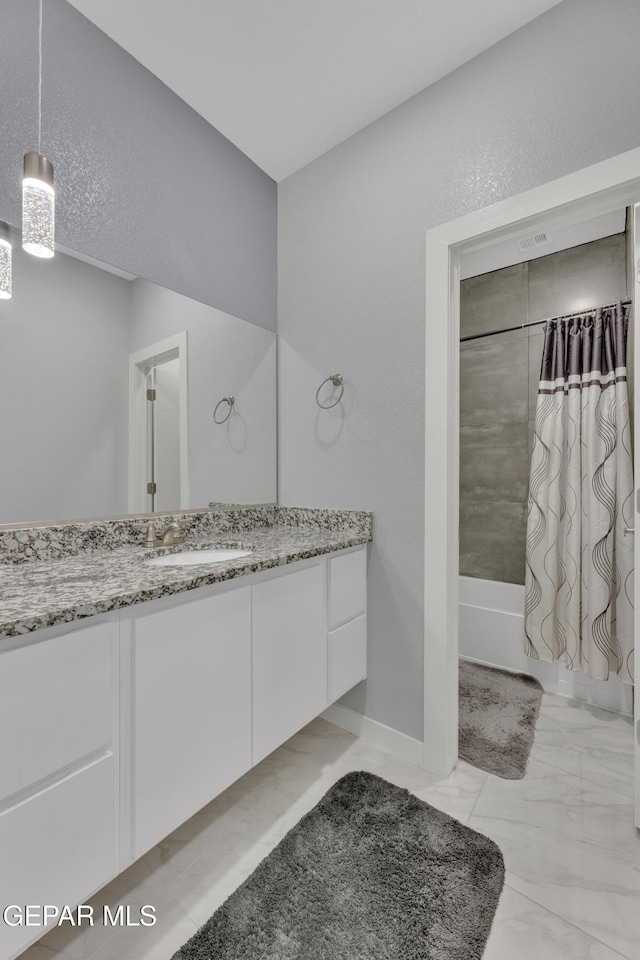 bathroom with marble finish floor, shower / bath combo with shower curtain, and vanity