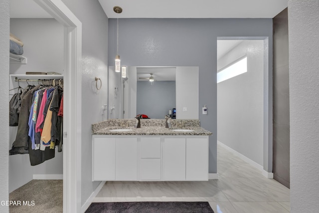 bathroom with a walk in closet, a sink, baseboards, and double vanity