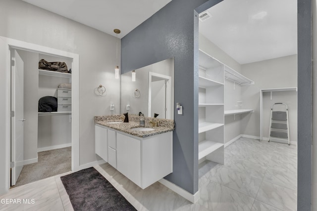 bathroom with visible vents, vanity, baseboards, marble finish floor, and a walk in closet