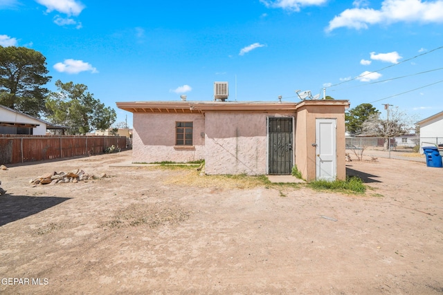 rear view of house featuring stucco siding, cooling unit, and fence