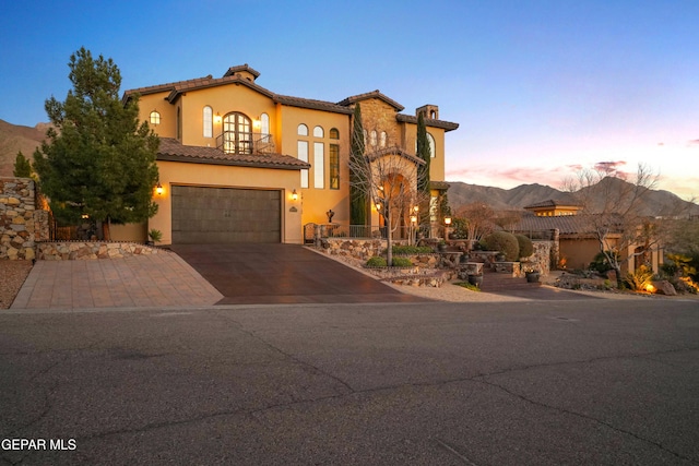 mediterranean / spanish house featuring aphalt driveway, stucco siding, a garage, a tile roof, and a mountain view
