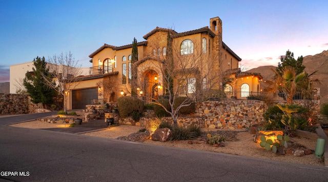 mediterranean / spanish-style house with a balcony, driveway, a chimney, stucco siding, and a tile roof