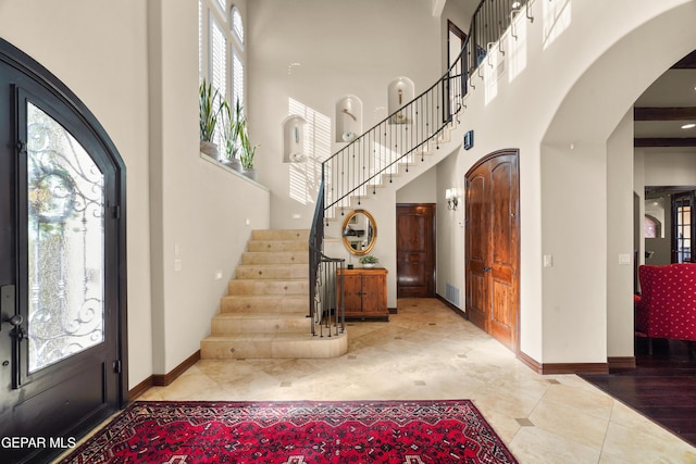 tiled entryway featuring visible vents, arched walkways, baseboards, a towering ceiling, and stairs