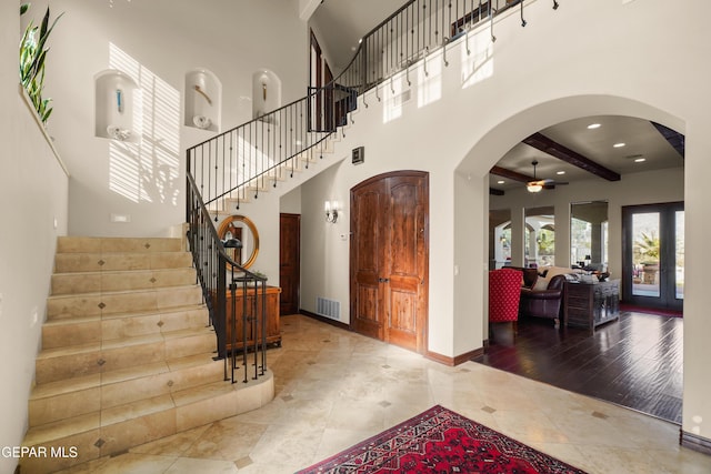 tiled foyer featuring visible vents, baseboards, stairway, arched walkways, and a ceiling fan