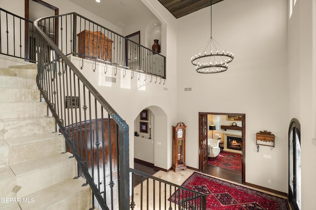 entrance foyer with visible vents, baseboards, arched walkways, a towering ceiling, and a notable chandelier