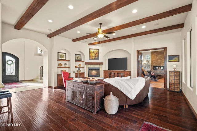 living room featuring arched walkways, a warm lit fireplace, hardwood / wood-style floors, and stairs