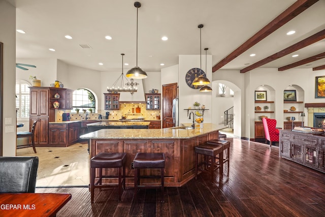 kitchen featuring beamed ceiling, open shelves, a sink, a kitchen breakfast bar, and decorative backsplash