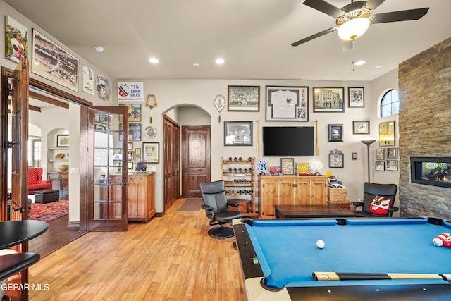game room with light wood-style flooring, arched walkways, and a wealth of natural light