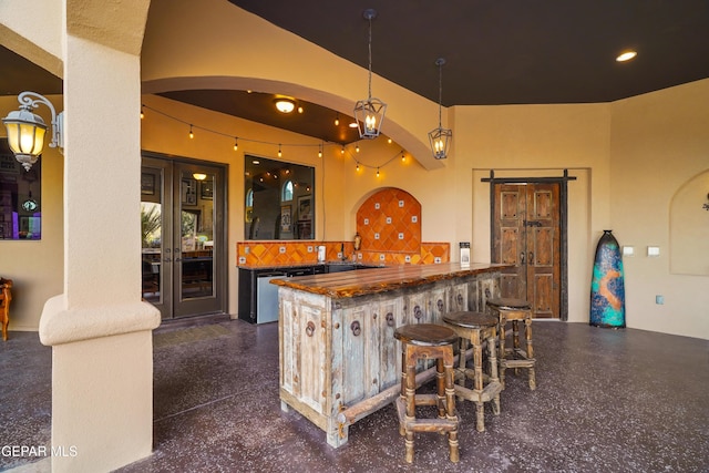 bar featuring backsplash, decorative light fixtures, dishwasher, wet bar, and arched walkways