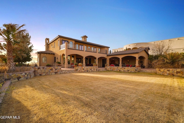 view of front of property with stucco siding, a balcony, a front yard, and a patio area
