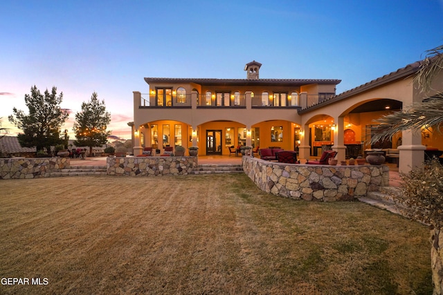 rear view of property featuring a balcony, a lawn, a patio, and stucco siding