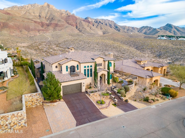 mediterranean / spanish-style house featuring stucco siding, decorative driveway, a mountain view, a garage, and a tiled roof