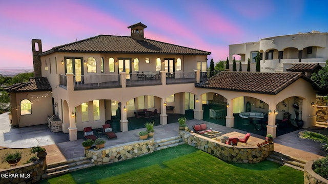 1408 Via Quijano Ln, El Paso, TX 79912 - back of house at dusk with a balcony, a patio area, stucco siding, and a chimney