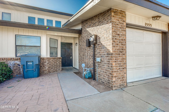 entrance to property featuring a garage and brick siding