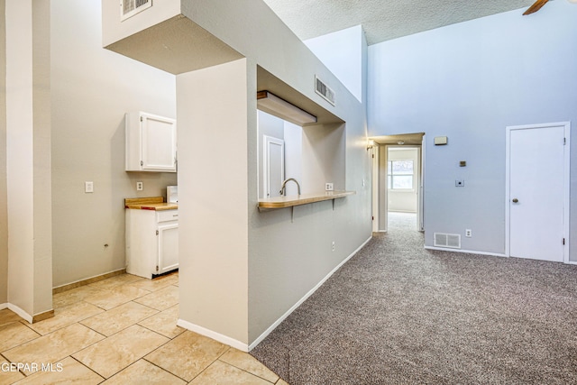 kitchen with visible vents, baseboards, light colored carpet, and white cabinetry