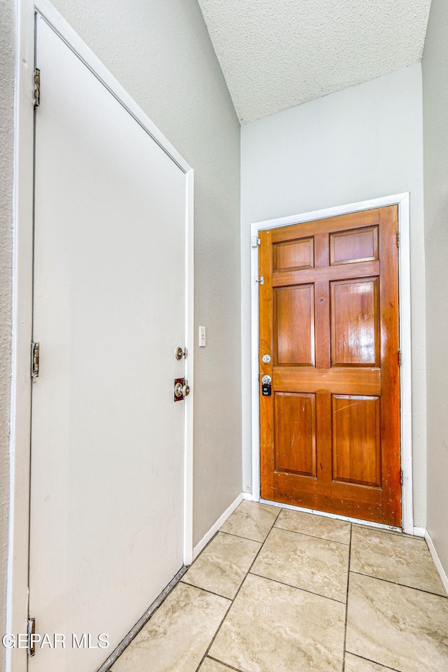 entryway with light tile patterned floors, a textured ceiling, and baseboards