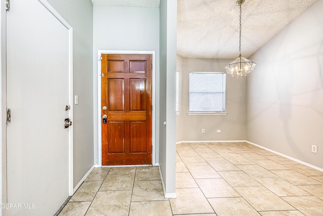 foyer entrance with light tile patterned floors, a chandelier, a textured ceiling, and baseboards