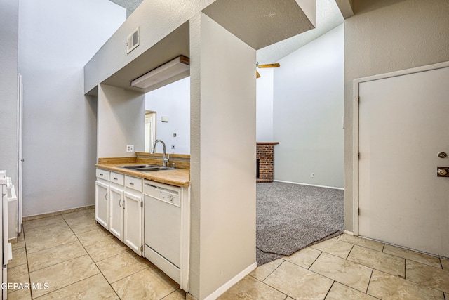 kitchen with a fireplace, white dishwasher, a sink, white cabinets, and light colored carpet