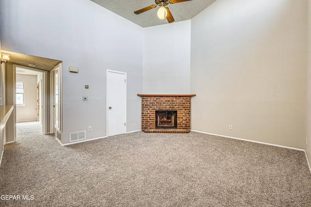 unfurnished living room with visible vents, a brick fireplace, baseboards, carpet, and a high ceiling