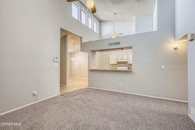 unfurnished living room with visible vents, a high ceiling, ceiling fan, a textured ceiling, and light colored carpet