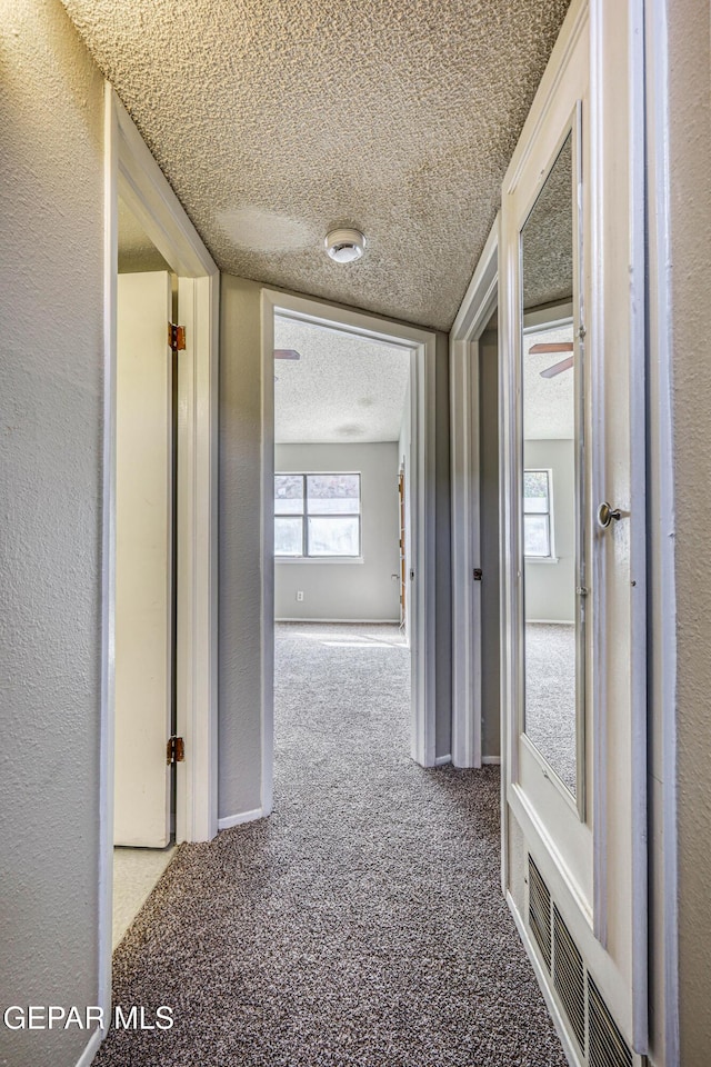 hall with visible vents, a textured ceiling, carpet flooring, and a textured wall