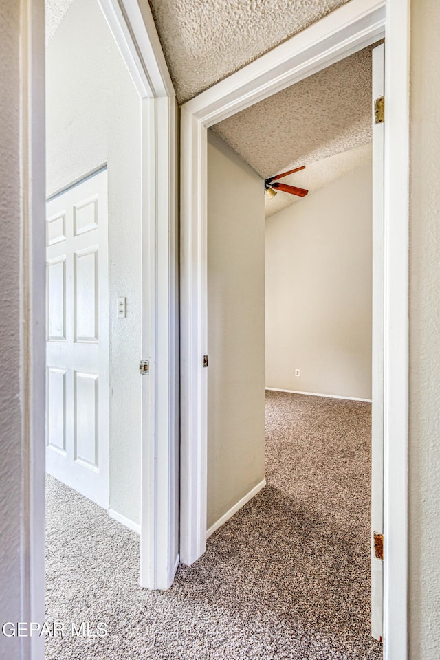 hallway with baseboards, a textured ceiling, and carpet