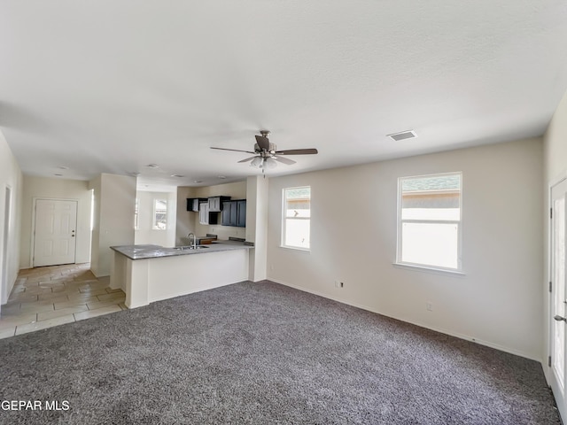 unfurnished living room with light tile patterned floors, visible vents, light carpet, ceiling fan, and a sink